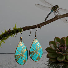 Load image into Gallery viewer, A pair of turquoise earrings with gold leaf designs hangs from a branch, accompanied by a dragonfly perched on the branch and a succulent plant in the background.