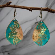 Load image into Gallery viewer, A pair of earrings with a floral design, featuring a combination of green and gold colors. The earrings are hanging from a branch, creating a natural and artistic setting.