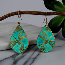 Load image into Gallery viewer, A pair of turquoise earrings with gold leaf designs, hanging from a wooden branch.