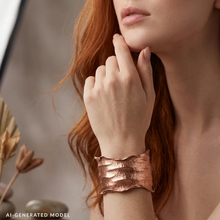 Load image into Gallery viewer, A close-up of a woman's hand wearing a copper-colored bracelet, with her hand resting on her chin.
