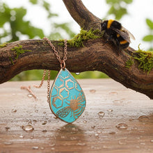 Load image into Gallery viewer, May include: A copper-colored necklace with a teardrop-shaped pendant. The pendant features a turquoise background with a honeycomb pattern and a bee design. A bumblebee rests on a branch in the background.
