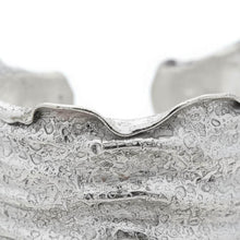 Load image into Gallery viewer, A close-up view of a textured, metallic bracelet or cuff with a rough, uneven surface.
