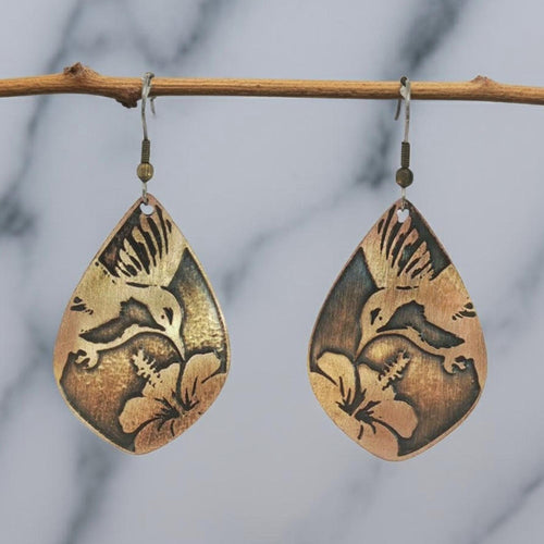 A pair of earrings with a bird and flower design, hanging from a wooden branch.