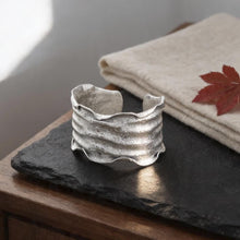 Load image into Gallery viewer, a silver cuff bracelet resting on a black slate, with a red maple leaf placed on a beige cloth nearby.
