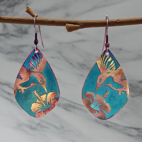A pair of colorful earrings with floral designs, hanging from a branch.