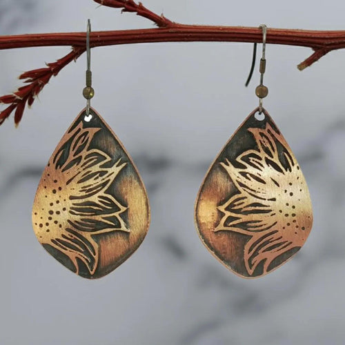 A pair of earrings with a floral design, hanging from a branch against a blurred background.