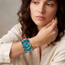 Load image into Gallery viewer, A woman with long, dark hair wearing a beige shirt and a turquoise and gold bracelet on her wrist.
