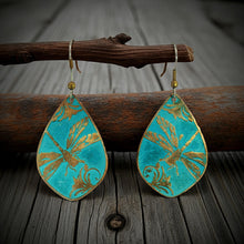 Load image into Gallery viewer, A pair of turquoise earrings with gold leaf designs, hanging from a wooden branch.
