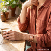 Load image into Gallery viewer, A person wearing a red shirt is sitting at a wooden table, holding a cup and resting their hand on their chin.
