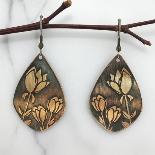 A pair of earrings with a floral design, featuring a combination of green and brown tones. The earrings are hanging from a branch, creating a natural and artistic appearance.